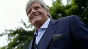 Uomo maturo con capelli grigi in abito blu, sorride all'aperto