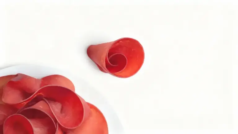 Fette sottili di bresaola disposte su un piatto bianco e una arrotolata accanto