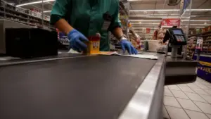 Una persona al lavoro alla cassa di un supermercato con guanti blu
