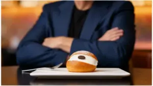 Maritozzo con panna servito su un piatto di ceramica, davanti a una persona in abito scuro