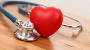 Cuore rosso e stetoscopio su tavolo in legno, simbolo di salute cardiovascolare