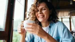 Persona che sorseggia un caffè sorridendo vicino a una finestra
