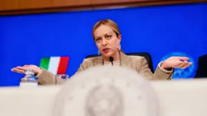 Una persona parla in conferenza stampa davanti a un microfono con sfondo blu