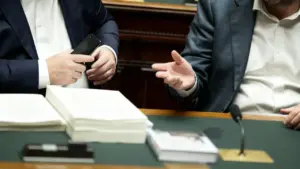 Due persone in abiti formali discutono accanto a documenti su un tavolo istituzionale