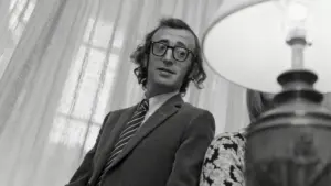 Persona con occhiali e cravatta a righe in un ambiente interno con tende leggere sullo sfondo