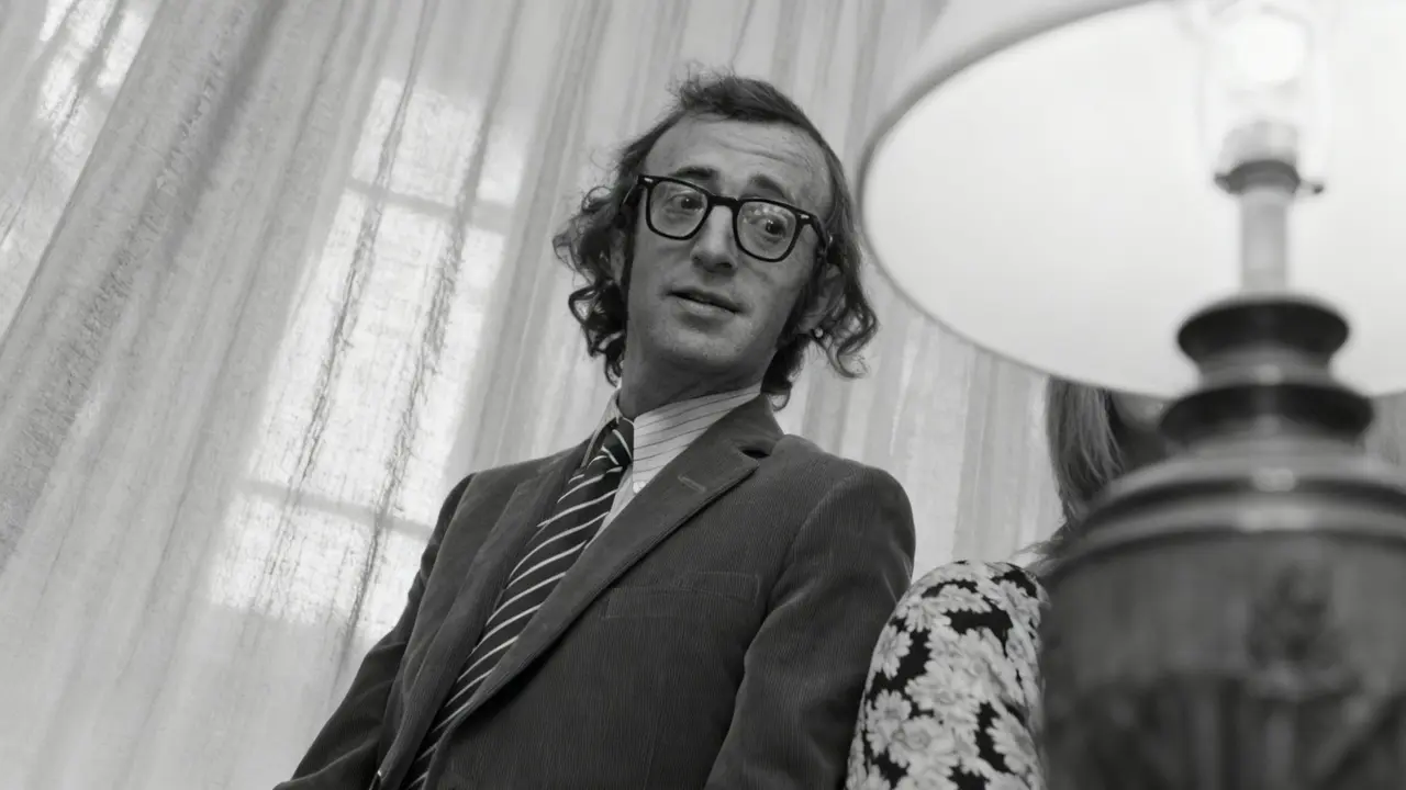 Persona con occhiali e cravatta a righe in un ambiente interno con tende leggere sullo sfondo