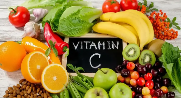 Frutta e verdura ricca di vitamina C disposta attorno a una lavagna su un tavolo di legno chiaro