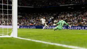 Un calciatore tenta di segnare mentre il portiere avversario prova a parare in uno stadio gremito