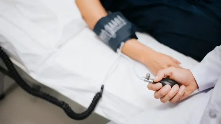 Persona distesa su un letto mentre un medico misura la pressione arteriosa con uno sfigmomanometro