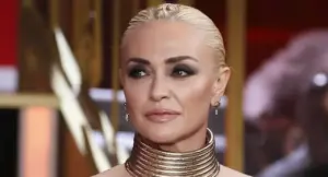 Una donna con capelli biondi raccolti e trucco marcato in un ambiente elegante