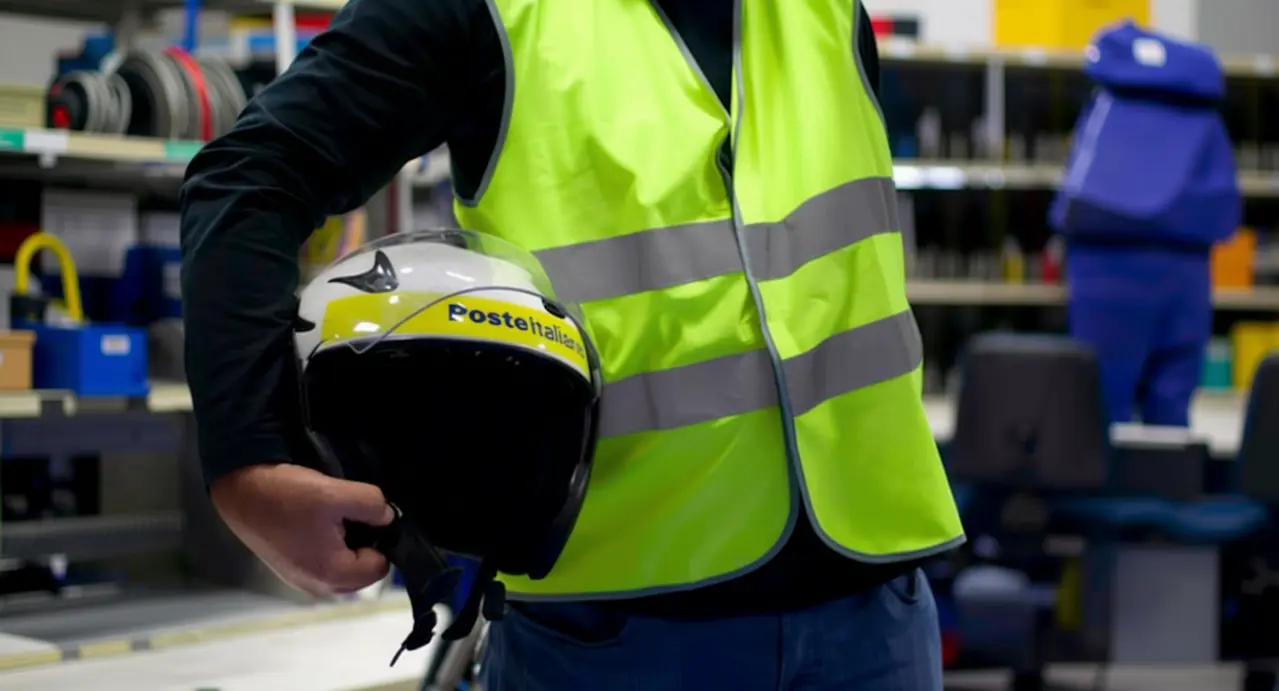 Persona con giubbotto riflettente che tiene in mano un casco Poste Italiane