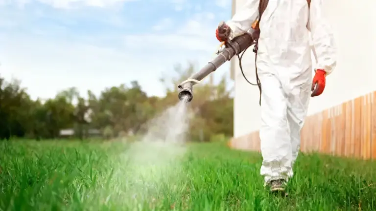 Persona con tuta protettiva che spruzza diserbante su un prato verde