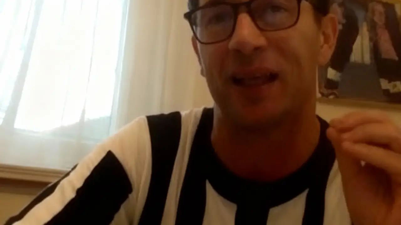 Una persona con occhiali e maglia bianconera parla in un ambiente interno