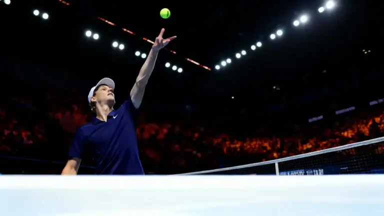 Tennista al servizio durante una partita su campo indoor illuminato