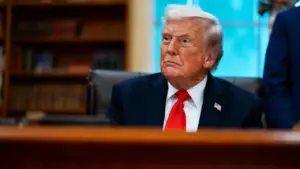 Una persona in giacca e cravatta rossa seduta a una scrivania con libreria sullo sfondo