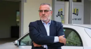 Uomo in giacca davanti a un edificio con un'auto bianca parcheggiata