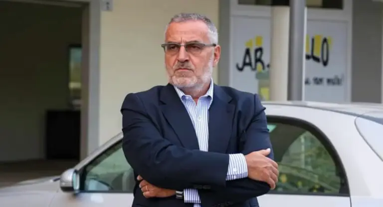 Uomo in giacca davanti a un edificio con un'auto bianca parcheggiata