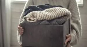 Persona con maglioni di lana piegati in una scatola di tessuto