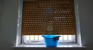 Secchio blu con panno sotto una tapparella parzialmente abbassata