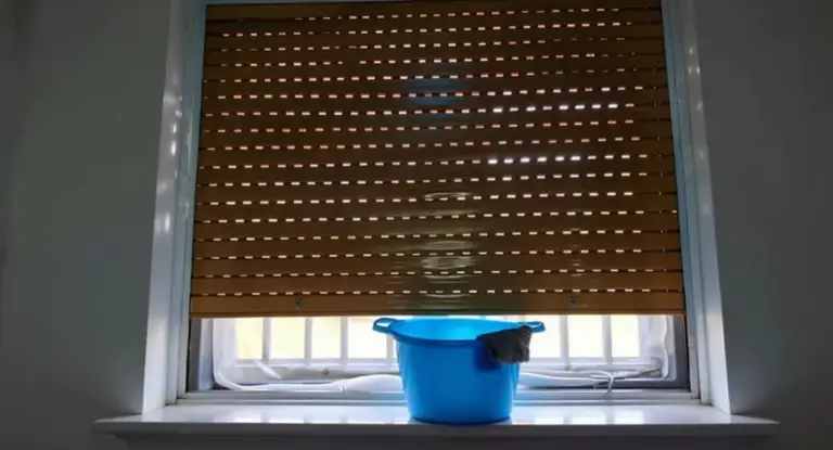 Secchio blu con panno sotto una tapparella parzialmente abbassata