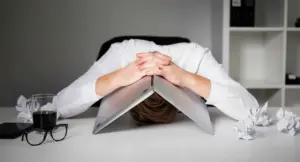 Persona con la testa abbassata su un laptop chiuso, circondata da fogli accartocciati