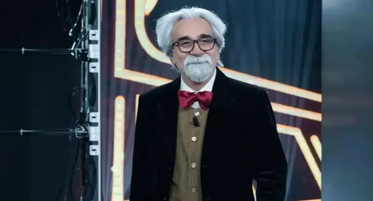 Una persona con capelli bianchi e barba indossa un completo elegante con papillon rosso