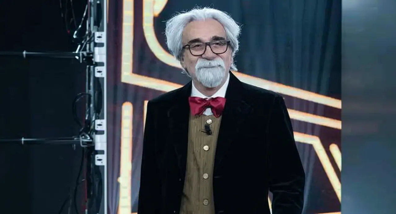 Una persona con capelli bianchi e barba indossa un completo elegante con papillon rosso