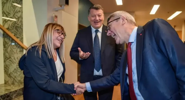 Tre persone in abiti formali si salutano cordialmente in un ambiente interno