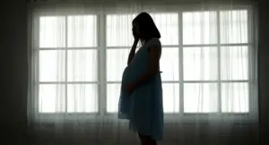 Donna incinta in silhouette davanti a una finestra, con una mano sulla pancia