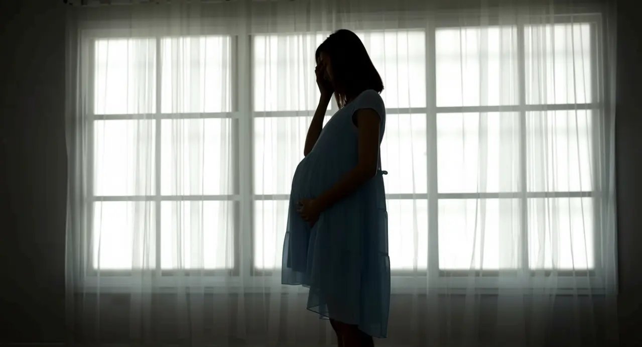 Donna incinta in silhouette davanti a una finestra, con una mano sulla pancia