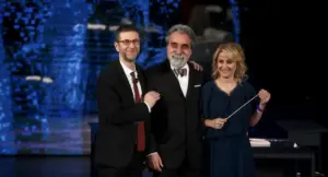 Tre persone sorridenti in abbigliamento elegante su un palco televisivo